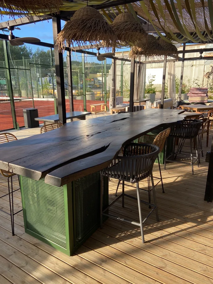 Long dark natural-edge bar table with open timber features on green bases