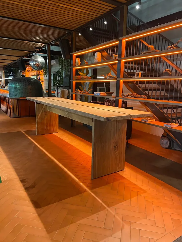 Long two-section wooden table with wooden panel legs in a warm interior