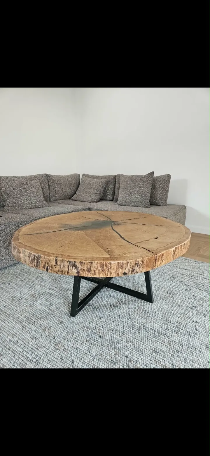 Round wood cross-section coffee table on a black metal base beside a grey sofa
