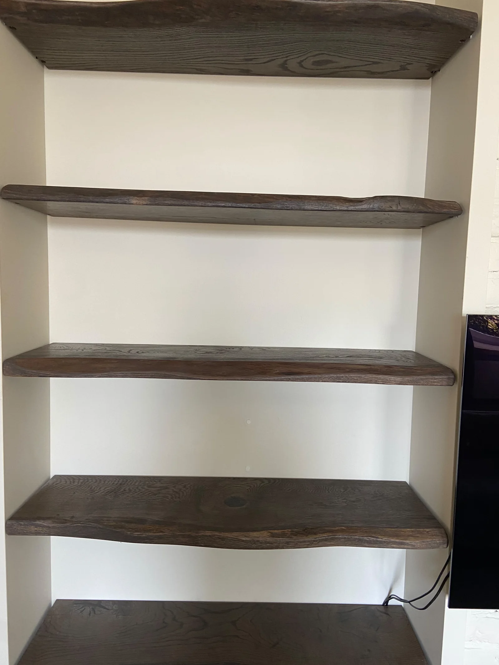 Dark natural-edge wooden floating shelves fitted into a white alcove